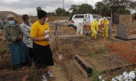 A family at a cemetery in Harare, Zimbabwe watch pallbearers carry the coffin of a relative who died from Covid-19