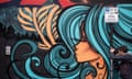 A man takes a photograph of a piece of street art featuring a profile of a woman with turquoise curls
