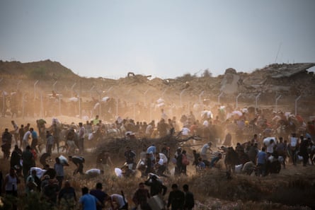 A large crowd of people scramble for bags amid a scene of buildings reduced to rubble