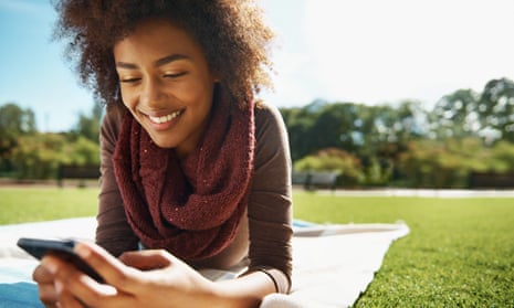 Shot of a smiling young woman relaxing with her phone in the park