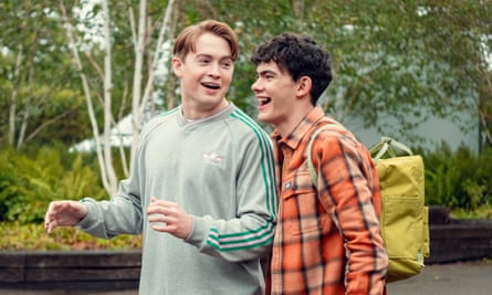Two teenagers walking and laughing, one wearing a green top and the other a check shirt and a backpack
