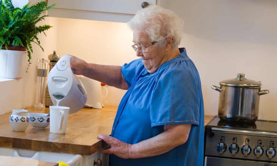 Lady in kitchen making tea using a kettle.