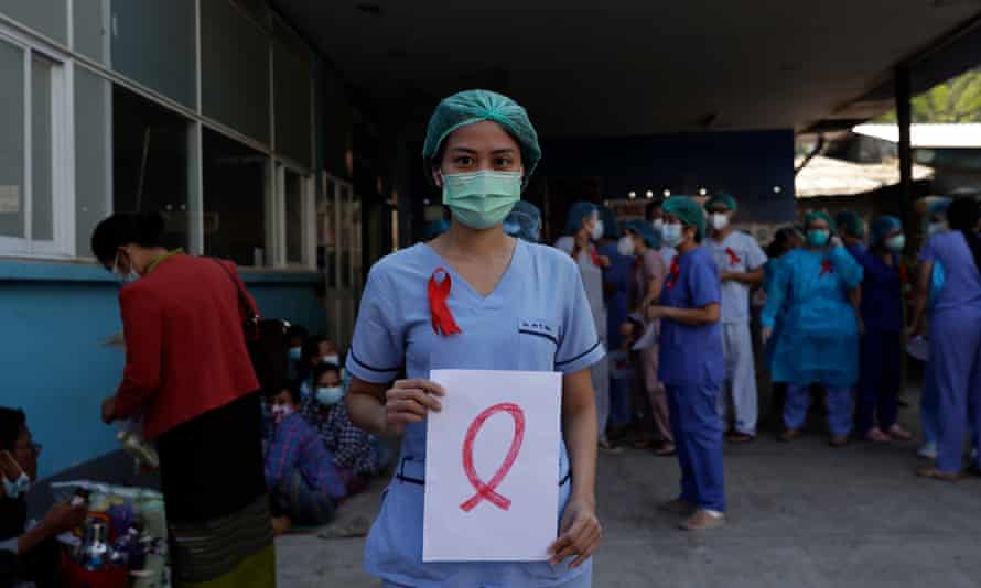 A member of medical staff wearing a red ribbon on her uniform holds a sign as a symbol of resistance against the military coup in Myanmar