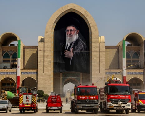 Red emergency vehicles outside the mosque which displays a large portrait of Khamenei