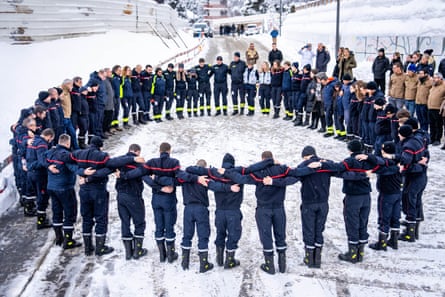Firefighters and emergency responders stand in a large circle outdoors with their arms around each other