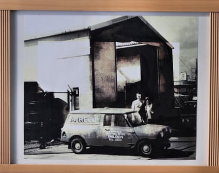 A black and white photo of Michael’s mother and father smiling outside a high garage with a small vehicle in front