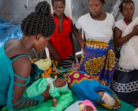 Four African women with small babies wait in a tent