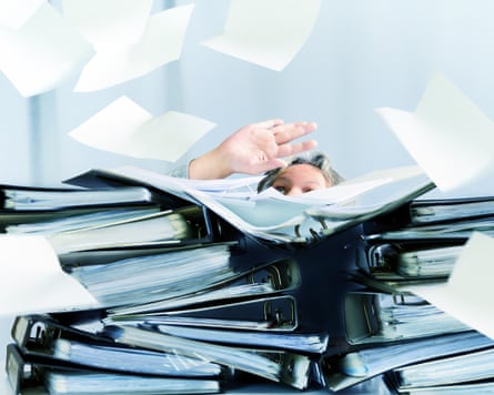 A woman behind high stacks of ring binders and lots of papers are flying around