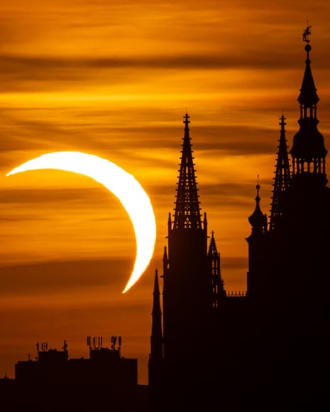 A crescent-shaped partial solar eclipse glows beside Prague Castle's silhouetted spires at sunset