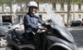 François Hollande wearing a dark suit and white helmet sitting on a scooter