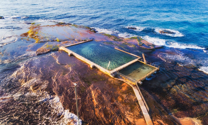 Remote isolated rock pool off Mona Vale beach at high tide with swimmer breaking waves of Pacific ocean coast in Sydney.
