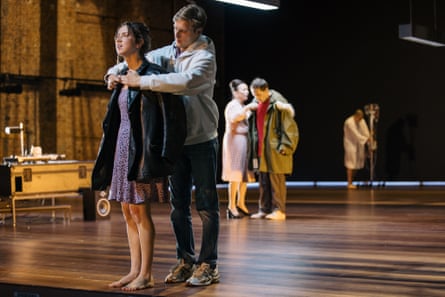 Angels in America. Two pairs of actors on stage, in each tableau one is helping the other off with their coat. At the rear, a hospital patient walks with a drip on a stand