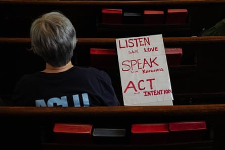 A person sits in a church pew beside a sign reading âÂÂListen with love, speak with kindness, act with intention.âÂÂ