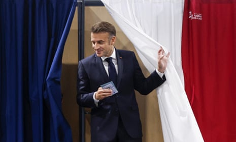 Emmanuel Macron emerging from a booth with ID documents in hand, through a tricolour curtain.