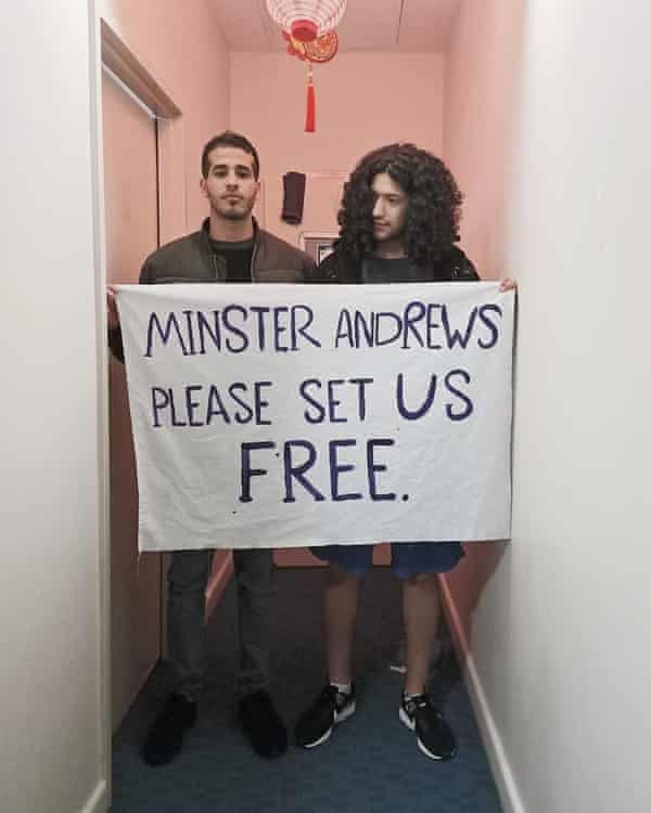 Two young Iranian asylum seekers standing in a hallway. They are holding a sign that says "Minister Andrews, please set us free."
