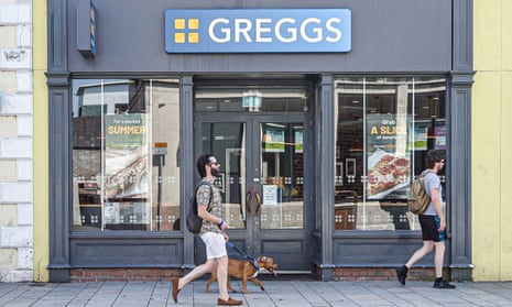 Man with a dog walks by Greggs store