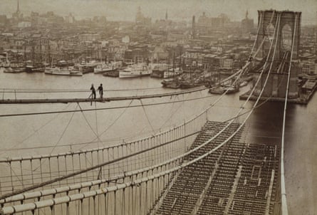 Two men survey the construction of the Brooklyn Bridge with Manhattan in the background, 1877.