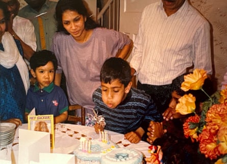 A dark-haired boy blowing out candles on a birthday cake surrounded by his family