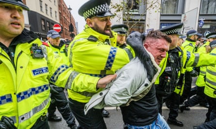 Stephen Yaxley-Lennon (Tommy Robinson) being pushed forward by police officers who have hold of his jacket and shoulders and are removing him from the area