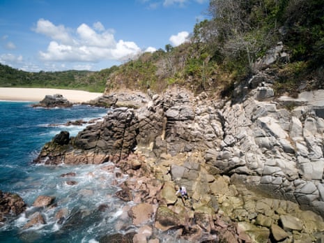 A man walks along a rocky shore next to a sandy beach