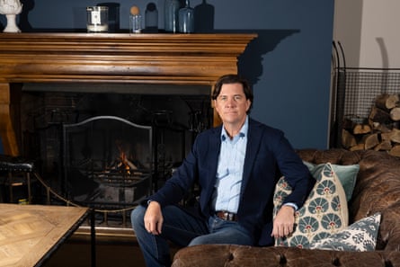 Man sits on a couch leaning on cushions in a room with a fireplace in the background