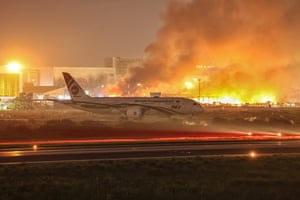 A passenger plane on a runway at night as a building behind it burns
