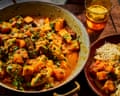 A pan of chicken and squash curry beside rice and a glass of beer