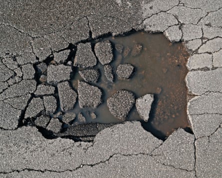 Close up photo of a pothole where the road surface is cracking into small pieces and a water-filled hole is forming