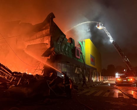 Firefighters battle a blazing, collapsed shopping centre in Kyiv at night using ladder truck hoses