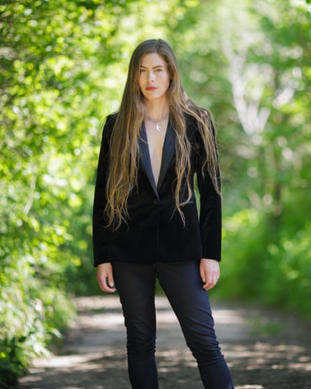 Young woman wearing a suit standing in a sunny wood posing for the camera.