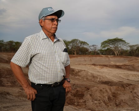An older Hispanic man stands amid levelled-off earth looking away