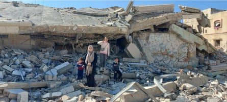 A woman and three children stand in the rubble of a bombed building.