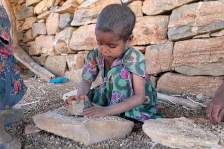 A child grinds down berry pits on a stone