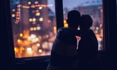 A silhouette of a couple embracing at dusk as they looking out a window onto a cityscape