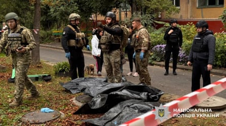 Police officers standing next to the bodies of people lying on the ground in black body bags