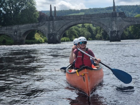 People in canoe on a wide river with old bridge behind them