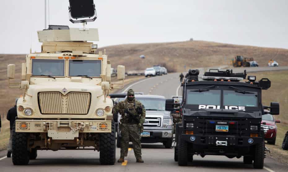 North Dakota law enforcement officers stands next to two armored vehicles just beyond the police barricade near a Dakota Access Pipeline construction site.