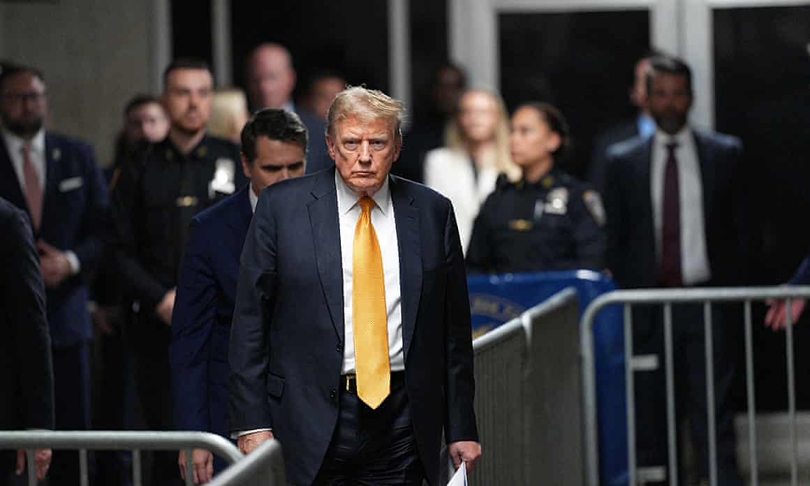 Donald Trump in yellow tie and suit with people behind him