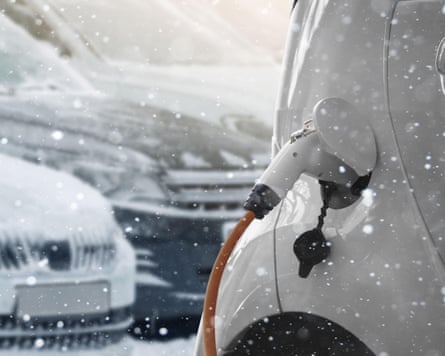 Close up of electric car with a connected charging cable on the blurred background of a snow covered parked cars.