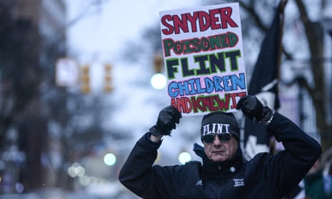 A protester poses for photo with his sign about Flint’s water crisis. Michigan governor Rick Snyder has been accused of ignoring concerns over quality of the city’s water supply.