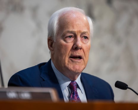 John Cornyn, an older man wearing a blue suit, speaks into a microphone on a desk