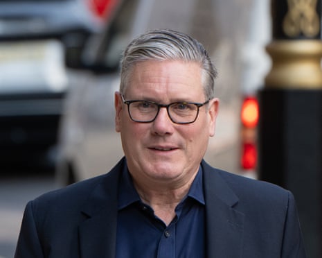 Keir Starmer in glasses wearing a dark suit and navy shirt smiles at the camera