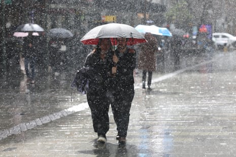 People use an umbrella to shelter from the rain as they walk along a Sydney CBD street