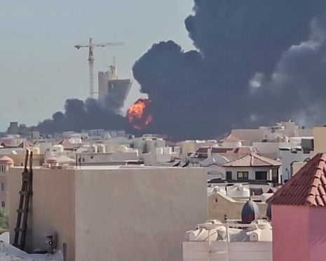 Large plumes of black smoke rise above Mangaf with orange flames visible at the base