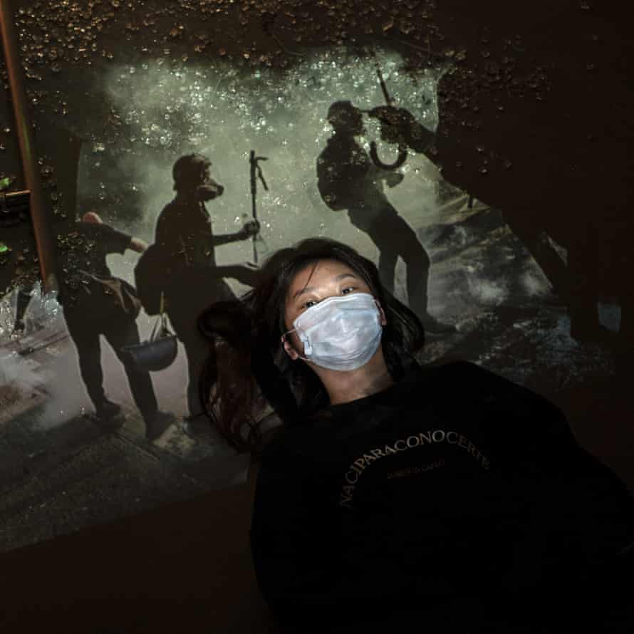 A protester, who identified herself as Morty, poses next to broken glass as a projector displays a photograph, taken during the unrest in Hong Kong.