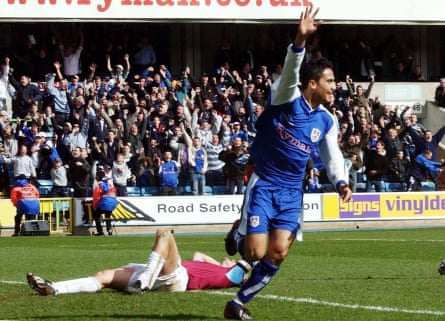 Tim Cahill raises his right arm while Christian Dailly lies on his back as Millwall fans celebrate in the background