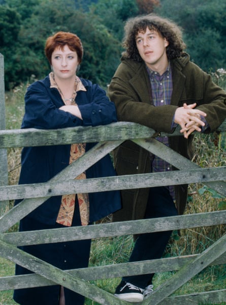 A man in a brown jacket and a woman in a blue coat standing behind a fence in a field