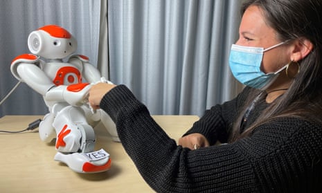 A Nao robot, a humanoid robot about 60cm tall, gives a fist=pump to a woman in a surgical mask