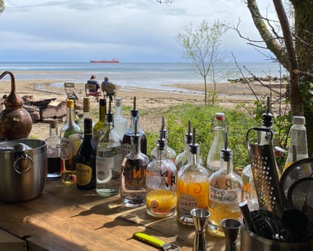 Looking out from behind a beach bar, the bar lined with spirit bottles, on to the sea with a red container ship on the horizon