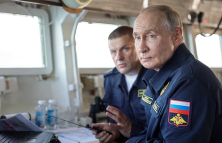 In naval fatigues, Vladimir Putin sits alongside Adm Vikot Liina on the bridge of a navy ship